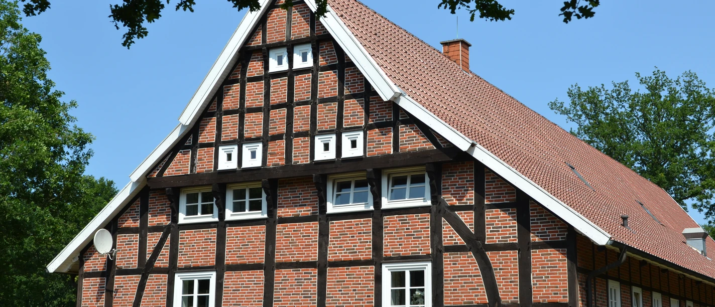 Heimathaus Vrees Historisches Fachwerkhaus mit rotem Ziegeldach, weißen Fensterrahmen und grünem Umfeld.