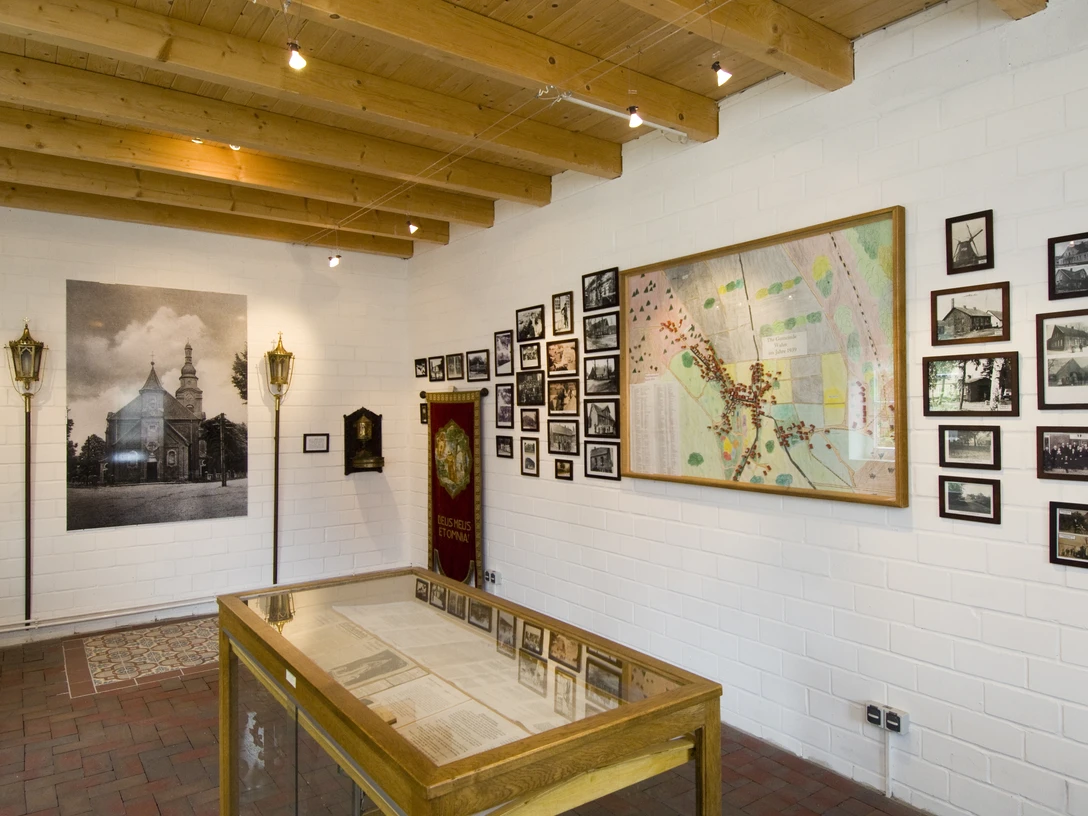 Wahner Zimmer Ausstellungsraum mit historischen Fotos, Karte, Vitrine und hölzerner Decke im Museumsdorf.