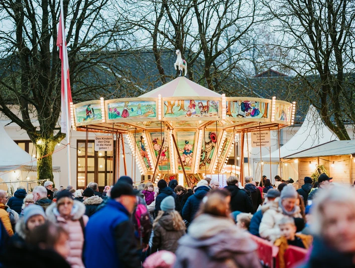 Ein nostalgisches Karussell auf einem Weihnachtsmarkt, umgeben von Menschen in Winterkleidung.