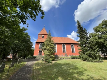 Rote Backsteinkirche in Kirchlinteln mit großem Kirchturm, umgeben von grünen Bäumen und Rasenflächen.