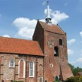 Ev.-ref. Kirche Groothusen Backsteinkirche mit hohem Turm und spitzem Dachhelm, roten Ziegeln und gotischen Fenstern unter blauem Himmel.