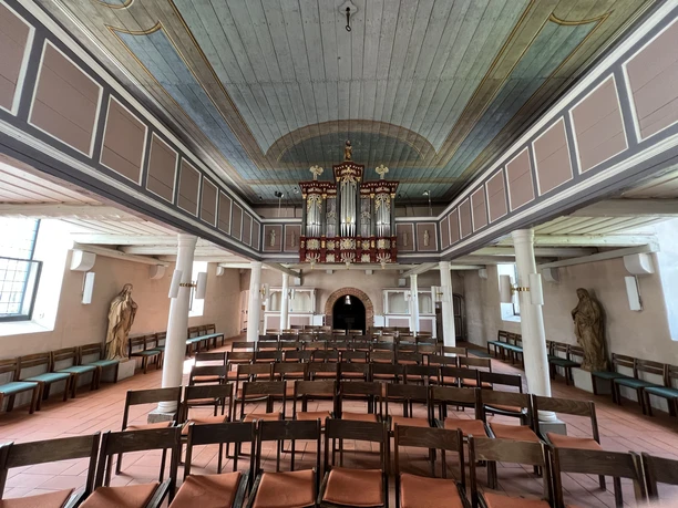 Lichtdurchflutetes Kircheninnere mit hölzerner Empore und prachtvoller Orgel über den Sitzreihen.