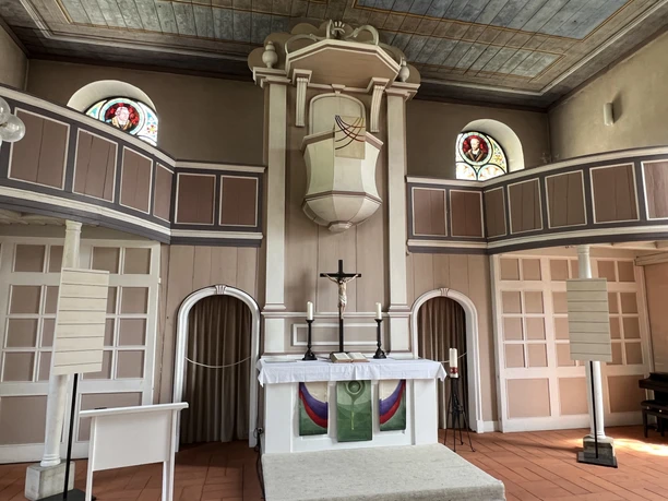 Kirche mit zwei Emporen, prächtigem Altar, aufwendiger Deckenverzierung und farbigen Glasfenstern.