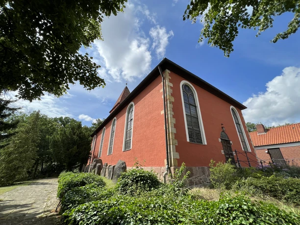 Klinkerfassade der St. Petri-Kirche Kirchlinteln, umgeben von grünen Bäumen und blauem Himmel.