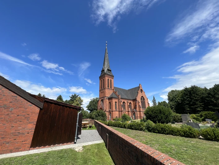 Die rote Backstein-St. Jakobi-Kirche in Wittlohe erhebt sich vor einem klaren blauen Himmel.