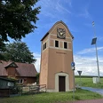 Glockenturm in Neddenaverbergen, Rotklinkerbau mit Uhr, umgeben von ländlicher Umgebung und blauem Himmel.