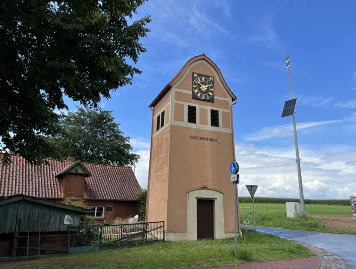Glockenturm in Neddenaverbergen Glockenturm in Neddenaverbergen, Rotklinkerbau mit Uhr, umgeben von ländlicher Umgebung und blauem Himmel.