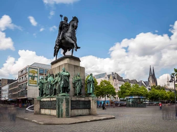 Kölner Altstadt Das Reiterdenkmal am Heumarkt in Köln zeigt eine imposante Darstellung eines Ritters in Rüstung auf einem Pferd, umgeben von einer Gruppe weiterer historischer Figuren. Der historische Stadtkern bildet die beeindruckende Kulisse.The equestrian monument on Heumarkt in Cologne shows an imposing depiction of a knight in armor on a horse, surrounded by a group of other historical figures. The historic city center forms the impressive backdrop.