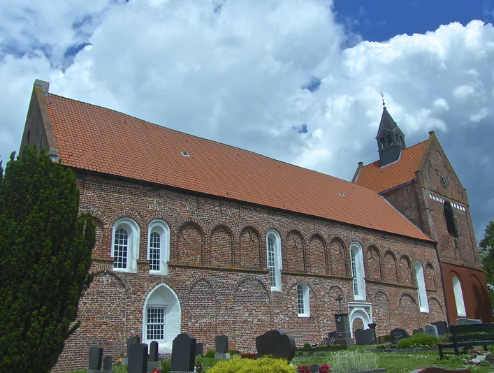 Evangelisch-reformierte Kirche Eilsum Backsteinkirche mit hohem Satteldach und Turm, umgeben vom Friedhof.