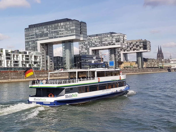 Kölntourist Personenschiffahrt Ein Ausflugsschiff namens 'RheinPerle' fährt vor der modernen Architektur der Kranhäuser in Köln.