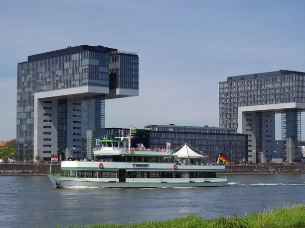 Kölntourist passenger boat service View of the Rhine in Cologne with a passing excursion boat in front of the striking crane buildings.