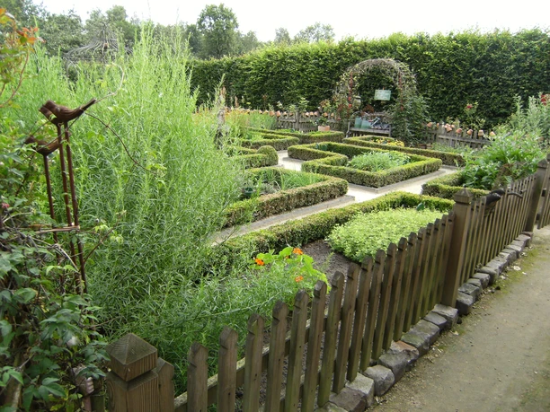 Kräuterhof Rosen Begrenzter Kräutergarten mit niedrigen Buchshecken, Wegen und Holzzaun im Grünen des Emslands