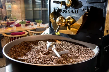 Kanne Rösterei Kaffeeröstmaschine mit frisch gerösteten Bohnen, im Hintergrund ein modern eingerichtetes Café.