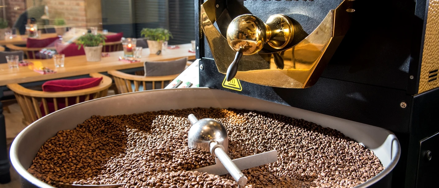 Kanne Rösterei Kaffeeröstmaschine mit frisch gerösteten Bohnen, im Hintergrund ein modern eingerichtetes Café.