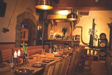Landhaus Brauerei Borchert Holzverkleideter Gastraum mit langen Tischen, Kupferlampen, gedecktem Tisch und Brauereiausrüstung.