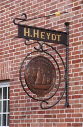 Private Kornbrennerei H. Heydt Metallschild der Kornbrennerei H. Heydt an roter Backsteinwand mit goldener Schrift und Relieflogo