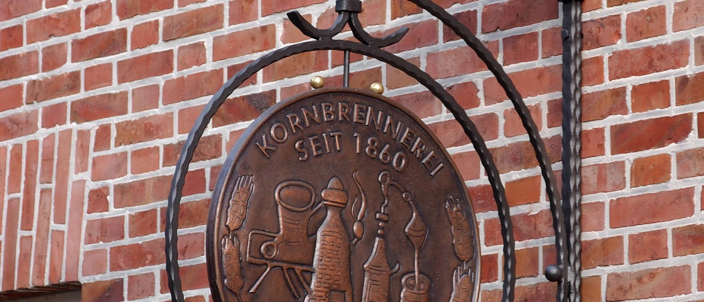 Private Kornbrennerei H. Heydt Metallschild der Kornbrennerei H. Heydt an roter Backsteinwand mit goldener Schrift und Relieflogo
