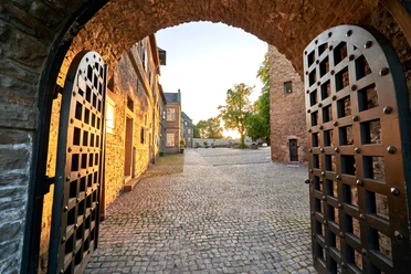 Schloß Broich, Mülheim an der Ruhr Blick durch ein geöffnetes Burgtor auf den gepflasterten Innenhof von Schloss Broich bei Sonnenuntergang.