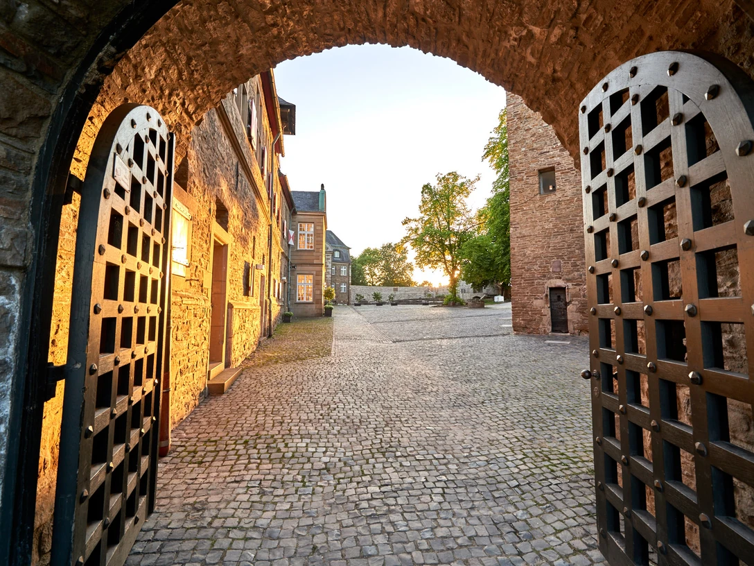 Schloß Broich, Mülheim an der Ruhr Blick durch ein geöffnetes Burgtor auf den gepflasterten Innenhof von Schloss Broich bei Sonnenuntergang.