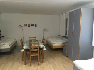 Monteurzimmer mit mehreren Betten, einem Tisch und Stühlen