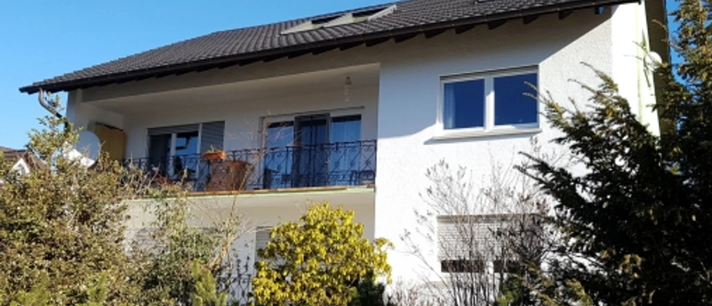 Außenansicht, weiße Fassade, umrahmt von Büschen und Bäumen