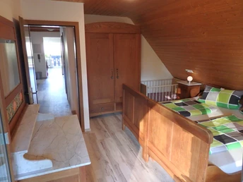 DG: Elternschlafzimmer. Mittelbraunes Holzbett mit karierter Bettwäsche, hinten Kleiderschrank. links Kommode