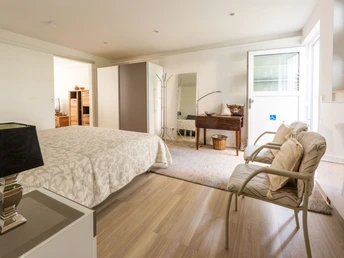 Schlafzimmer in Beigetönen mit Doppelbett, Kleiderschrank, Sekretär, zwei Stühlen, Nachttisch mit Lampe