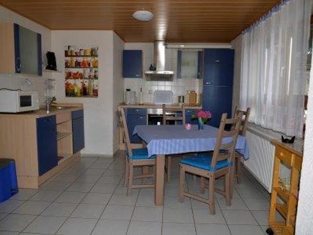 Einbauküche aus hellem Holz mit blauen Schranktüren. Im Vordergrund ein Esstisch mit Stühlen