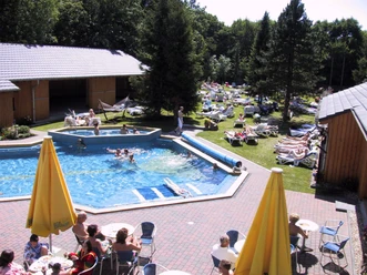 Roetgen Therme Außenpool Außenpool in sommerlichem Ambiente mit Personen auf Liegestühlen und Schwimmenden im Wasser, umgeben von Wiesen und Bäumen.