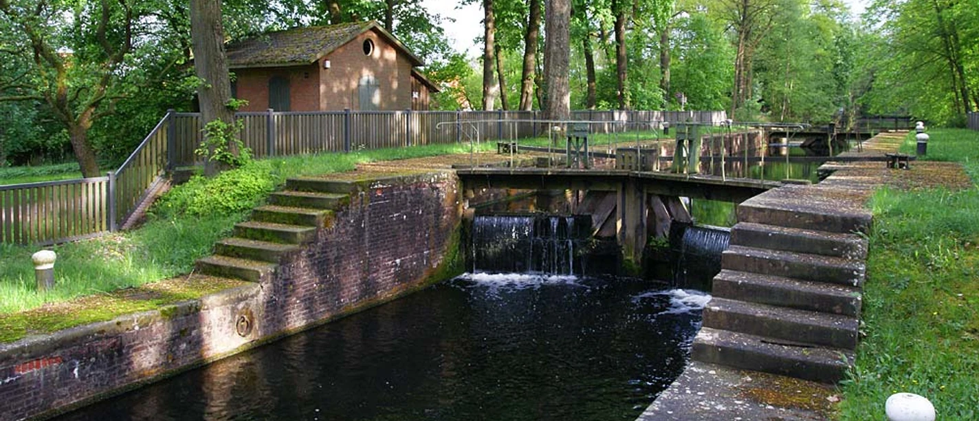 Koppelschleuse Historische Schleusenanlage mit Backsteinhaus, Wasserlauf und von Bäumen gesäumtem Grünbereich