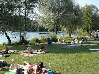 Liegewiese mit Menschen auf Handtüchern, Bäume am Rand vom See