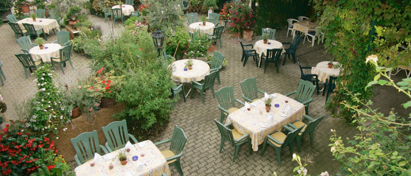 Blick auf die Gartenwirtschaft mit vielen Tischen, Stühlen, Blumen und frischen Kräutern