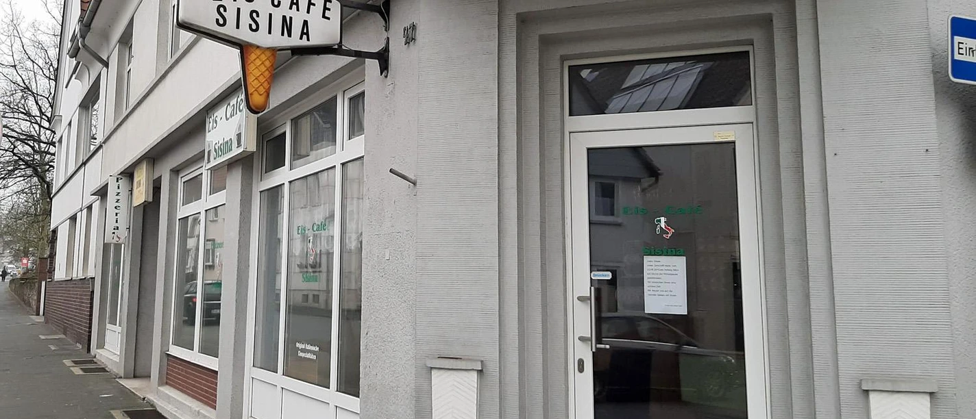 Eingang des Eiscafés Sisina mit großem buntem Eishörnchen-Schild an der Fassade