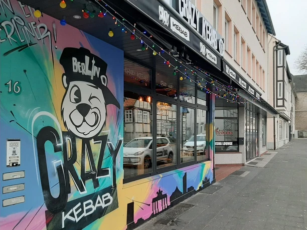 Bunte Graffiti-Fassade von Crazy Kebab mit Panda-Logo und Lichterkette am Gehweg