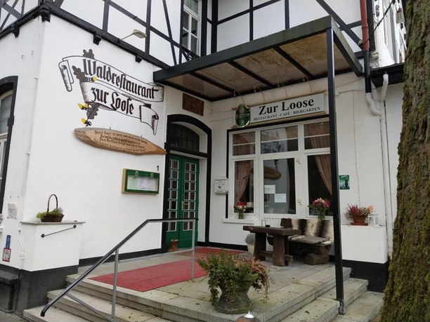 Eingang des Waldrestaurants Zur Loose im Fachwerkhaus mit grünen Türen und Sitzbank
