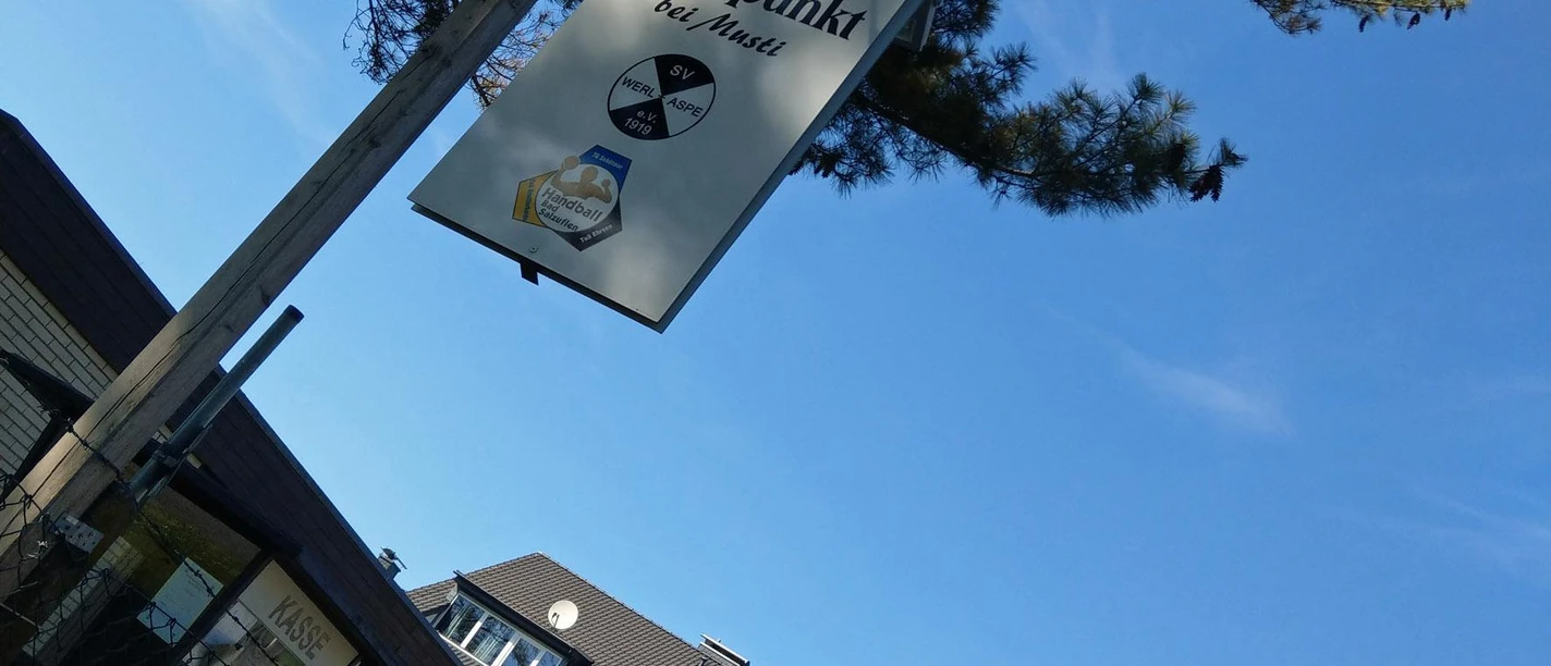Schild des Asper Treffpunkts bei Musti vor blauem Himmel und Baumkronen