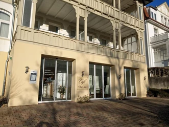 Eingang des Café Villa Luise mit Glasfront und Holzbalkonen in sonniger Hausfassade