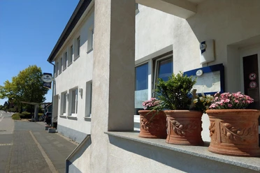 Außenansicht des Restaurant Olympia mit Blumenkübeln und Schild an heller Fassade