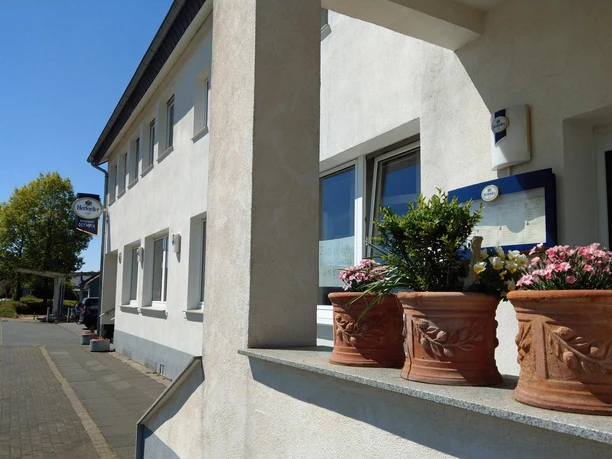 Außenansicht des Restaurant Olympia mit Blumenkübeln und Schild an heller Fassade