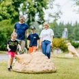 Tiere aus unseren Gärten und Siedlungen_besimmazhiqi-166.jpg Familie spaziert durch den Park, Kinder spielen fröhlich mit einem großen Kunstobjekt aus Stein.