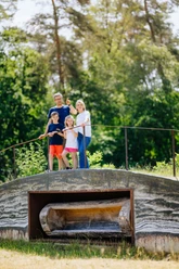 Archäologischer Erlebnispfad_besimmazhiqi-128.jpg Familie auf einem bewachsenen, hölzernen Unterschlupf inmitten eines Waldes, blickt lächelnd umher.