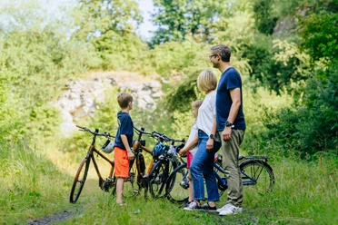 Familie mit zwei Kindern steht mit Fahrrädern in einem grünen Tal nahe eines alten Steinbruchs.