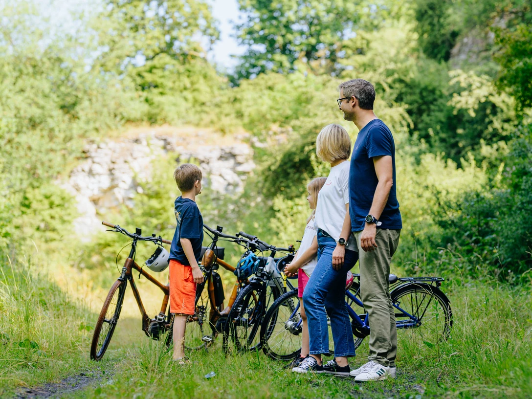 Steinbruch Langes Tal_besimmazhiqi-35.jpg Familie mit zwei Kindern steht mit Fahrrädern in einem grünen Tal nahe eines alten Steinbruchs.