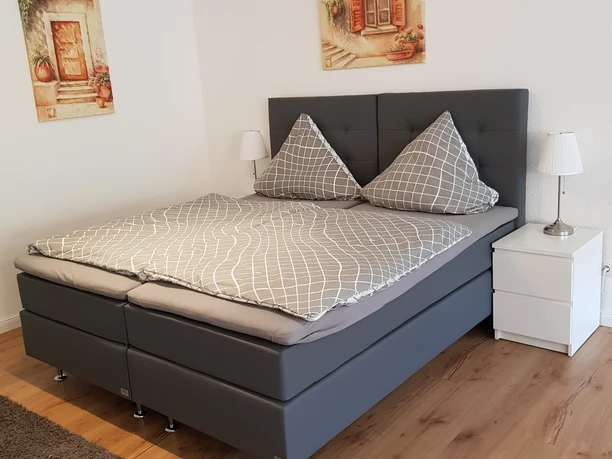 Helles Schlafzimmer mit Doppelbett, modernem Design, Holzfußboden und zwei Nachttischen mit Lampen.