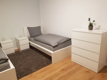 Helles, modernes Schlafzimmer mit Einzelbett, weißen Möbeln, Holzboden und minimalistischer Dekoration.