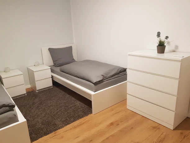 Helles, modernes Schlafzimmer mit Einzelbett, weißen Möbeln, Holzboden und minimalistischer Dekoration.