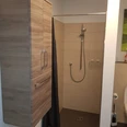 Barrierefreies Badezimmer mit ebenerdiger Dusche, Duschvorhang, Handbrause und Holzschrank.