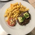 Rumpsteak belegt mit Kräuterbutter, dazu goldene Pommes und eine gefüllte Tomatenhälfte auf einem Teller.