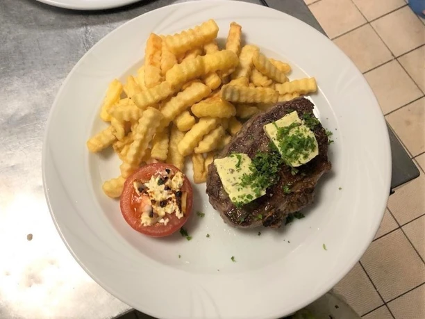 Rumpsteak belegt mit Kräuterbutter, dazu goldene Pommes und eine gefüllte Tomatenhälfte auf einem Teller.