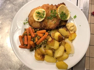 Schnitzel mit Zitronenscheiben, gebratenen Kartoffeln, Erbsen, Karotten und Senf auf einem weißen Teller.